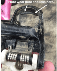 Close-up of a worn bike pedal, with arrows indicating an area of more wear on the upper edge and less wear on the lower edge.